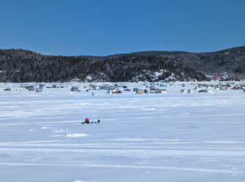 Le fjord du Saguenay enneigé avec des cabanes de pêche qu'on aperçoit au loin.