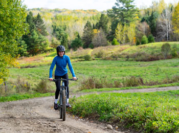 Une femme en vélo sur un sentier en terre dans un décor de début d'automne.