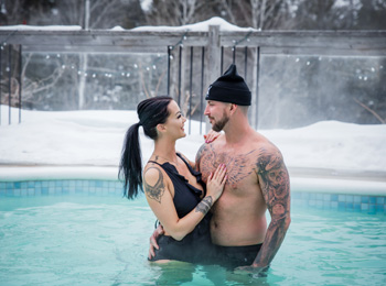 Jeune couple en maillots de bain dans la piscine extérieure l'hiver au AX Hôtel à Tremblant.