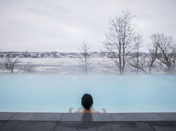 Vue de dos d'une personne dans un spa en train de regarder la vue sur le fleuve en hiver.