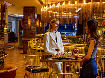 Deux femmes en train de prendre un verre de vin rouge dans un établissement de restauration aux accents dorés.