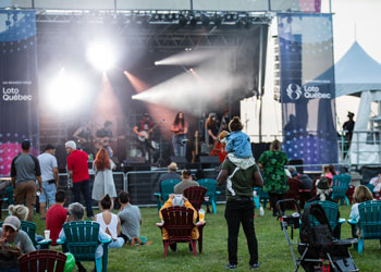 Parterre devant une scène de festival, avec chaises et familles.
