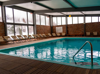 Piscine intérieure bordée de chaises dans une grande pièce fenestrée.