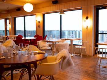 Intérieur d'un bistro aux allures chaleureuses, avec grandes fenêtres et beaucoup de luminosité.
