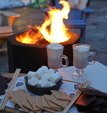Feu extérieur avec des tasses de chocolat chaud et les ingrédients pour faire des s'mores.