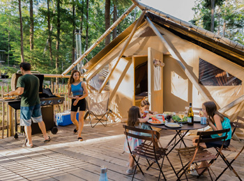 Famille de quatre personnes en train de profiter de la terrasse de leur prêt-à-camper sous le soleil.