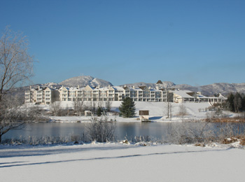 Extérieur du Manoir des Sables en hiver avec le lac en avant-plan et les montagnes derrière.