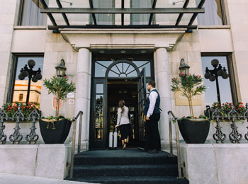 Devanture de l'hôtel; une femme traverse la porte aux côtés d'un portier.