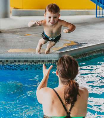 Mère dans la piscine d'hôtel qui attrape son fils qui saute dans l'eau.