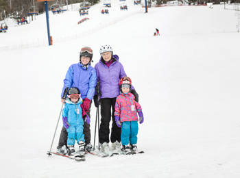 Mère, grand-mère et deux filles en habits de ski au pied de la pente.