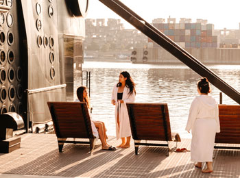 Trois femmes en peignoir sur la terrasse du spa, qui donne sur l'eau.