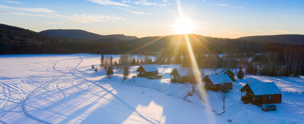 Vue aérienne de chalets sous la neige au bord d’un lac.