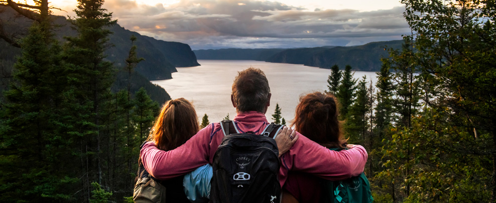 Trois personnes qui admirent le paysage de lac et de forêts.