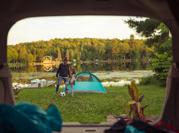 Une mère et sa fille en train de jouer au soccer à côté d’une tente au bord d’un lac.