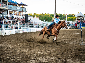 Femme dans une arène de rodéo sur son cheval devant le public.