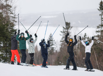6 skieurs et skieuses en haut de la montagne qui soulèvent triomphalement leurs bâtons.