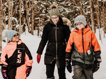 Une mère et deux enfants, tous souriants, dans une forêt enneigée.