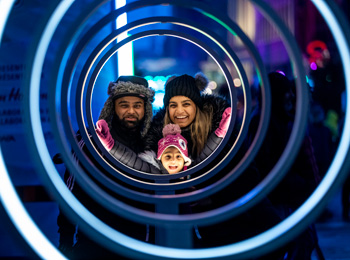 Père, mère et fillette souriants qui admirent une installation lumineuse au Bal de neige.