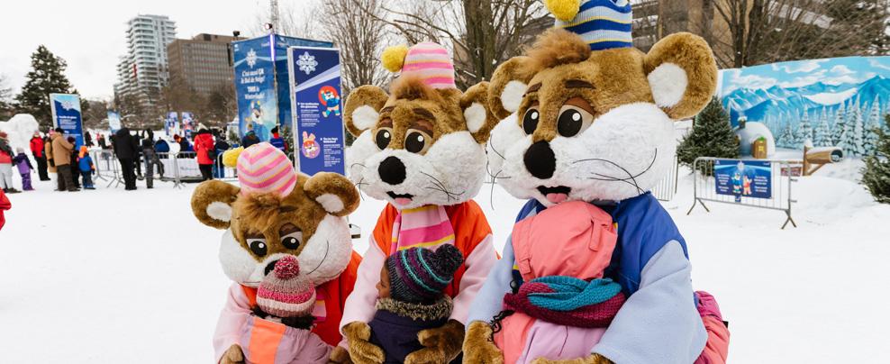 Trois mascottes dehors en hiver qui donnent des câlins à des enfants.