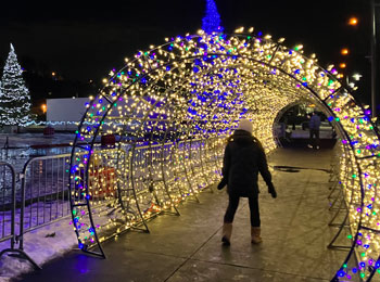 Femme en train de marcher sous une arche illuminée à l'extérieur.