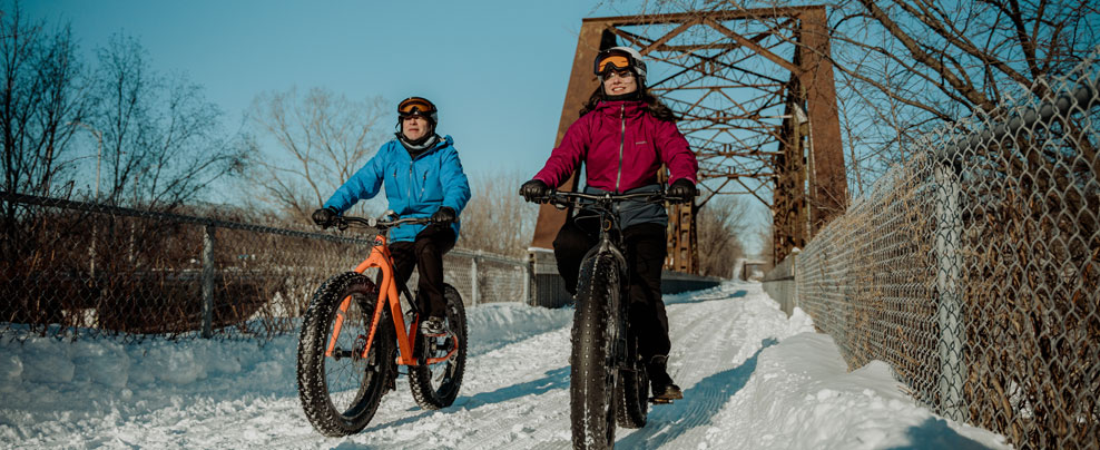 Deux personnes en fatbike sur une piste enneigée.