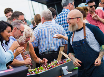 Exposant culinaire qui fait goûter des bouchées et la foule en arrière-plan.