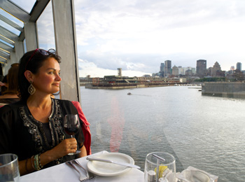 femme avec un verre de vin à bord d'un bateau de croisière qui admire la vue de Montréal.